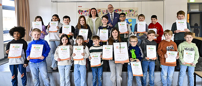 Eine Gruppe von Kindern steht aufgereiht und strahlend mit Urkunden in den Händen in einem hellen Raum.