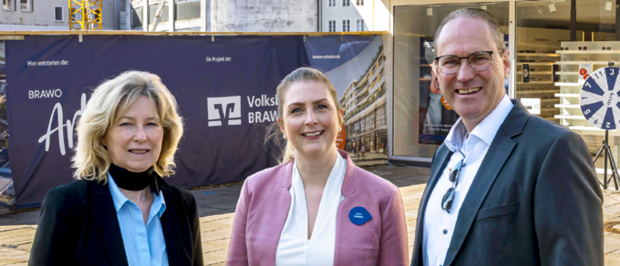 Drei Personen stehen vor den Brawo Arkaden in Wolfsburg, lächelnd in die Kamera, mit Bauarbeiten im Hintergrund.