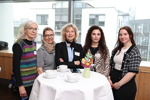 Fünf Frauen stehen um einen Tisch mit Kaffeetassen und Blumen, lächelnd in die Kamera in der Autostadt.