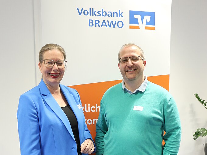 Zwei Personen lächeln vor einem Volksbank BRAWO Banner.