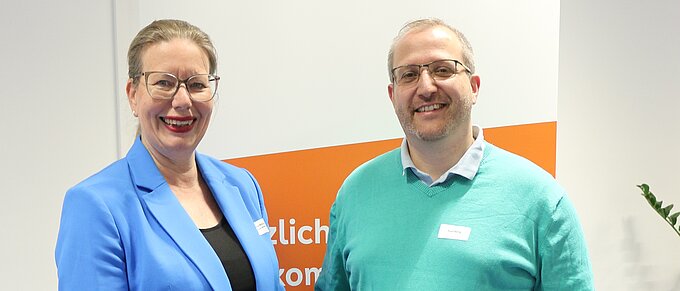 Zwei Personen lächeln vor einem Volksbank BRAWO Banner.